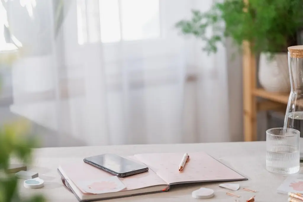 明るい部屋のデスクにプランナーとスマートフォンが置かれた穏やかな風景。Photo by Svitlana on Unsplash